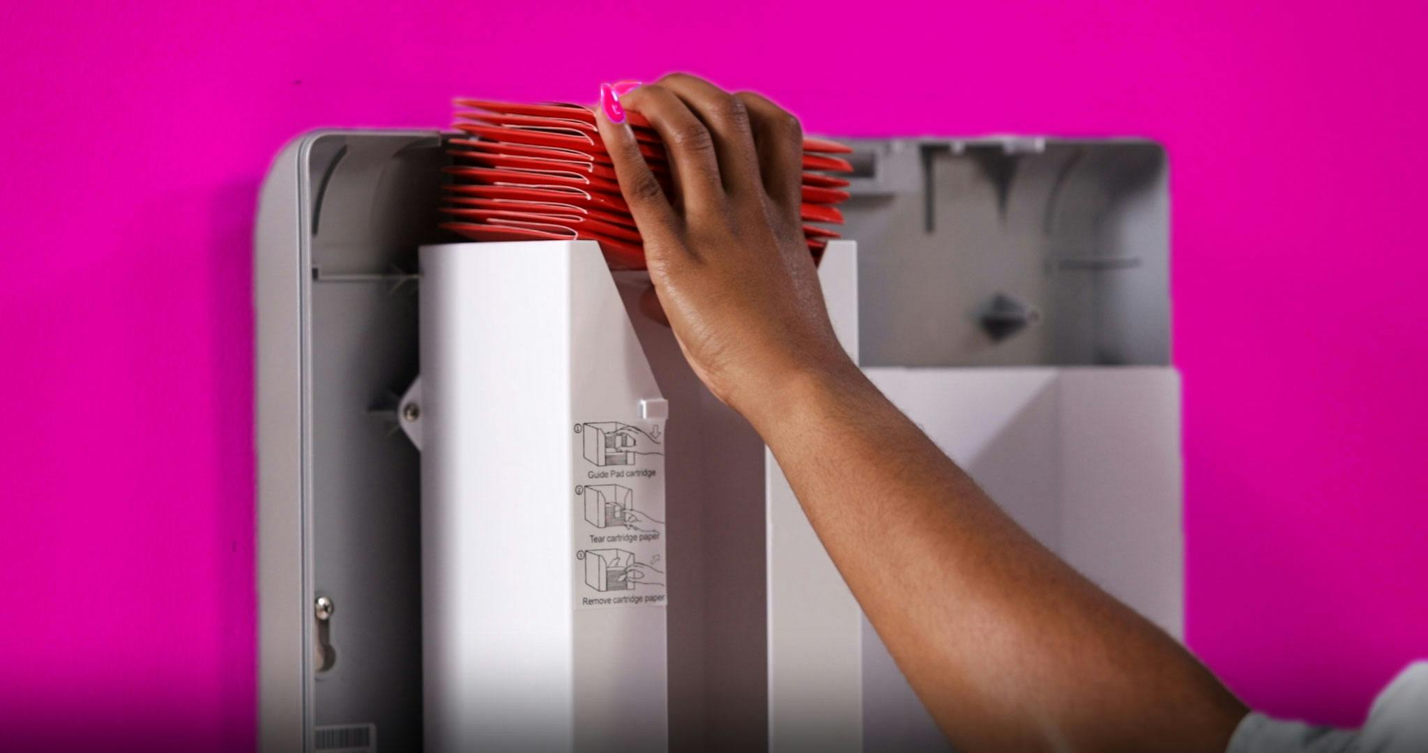 A hand with nail polish refilling a vending machine with menstrual pads