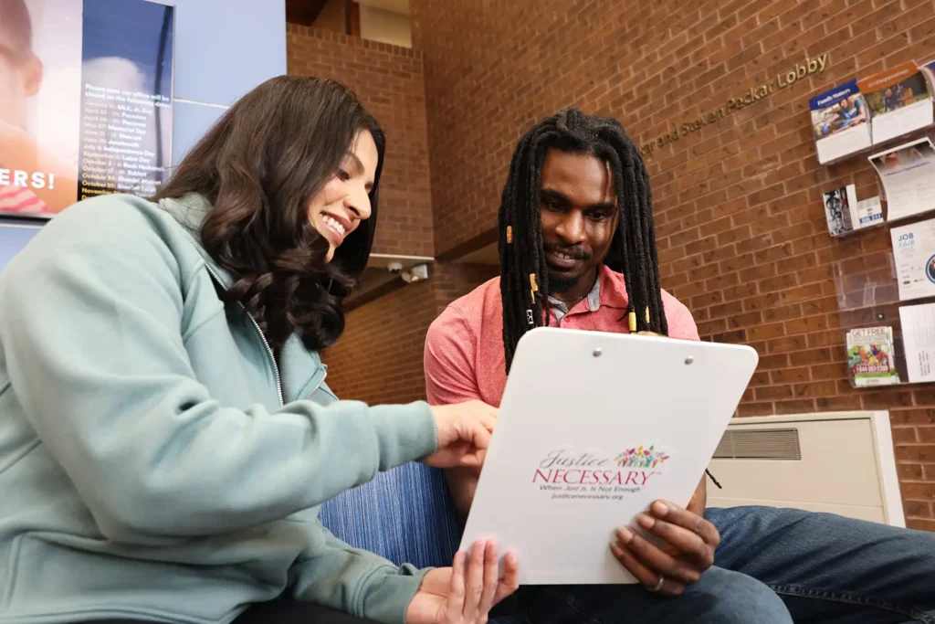 A man and a woman read a document being held in a Justice Necessary clipboard