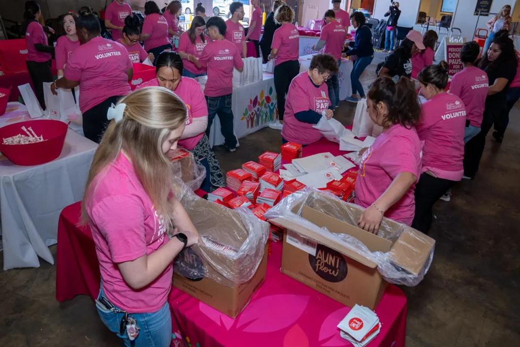 An overhead view of a period packing party with volunteers filling bags with hygiene supplies.