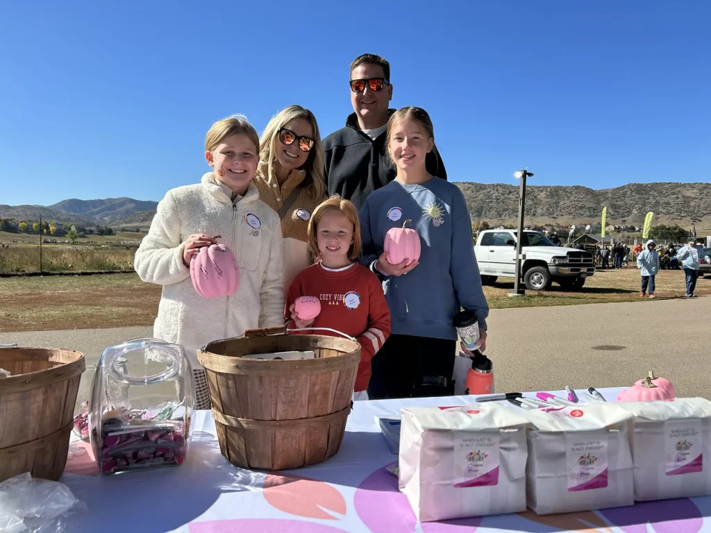 A family of volunteers holding pink painted pumpkins standing over a table of period products.